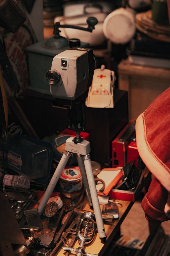 collection-05 A vintage camera on a tripod surrounded by assorted antiques in a cozy shop.