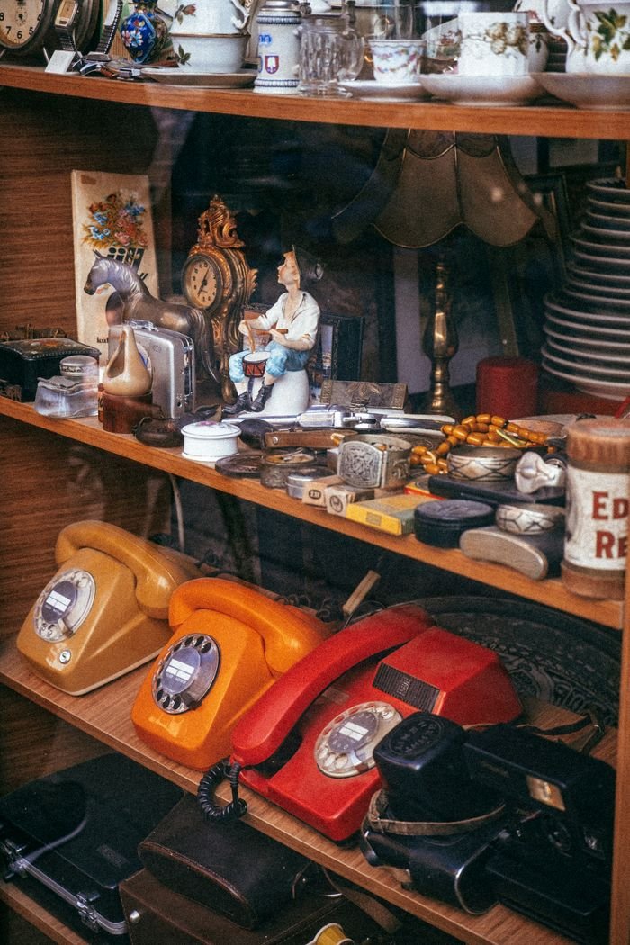 collection-04 A collection of vintage telephones and antiques on wooden shelves within an antique shop.