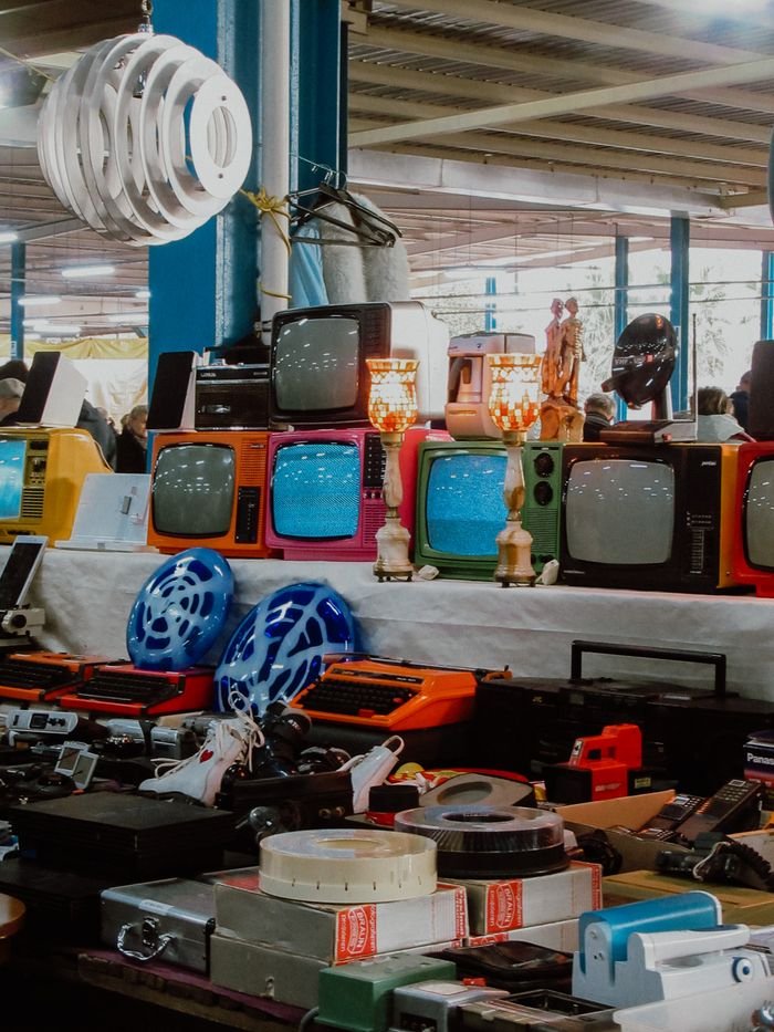 Colorful vintage TVs and electronics displayed at a bustling flea market.