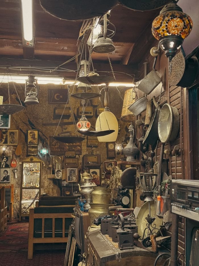 collection-01 A cozy antique shop filled with vintage items and historical decor under soft lighting.