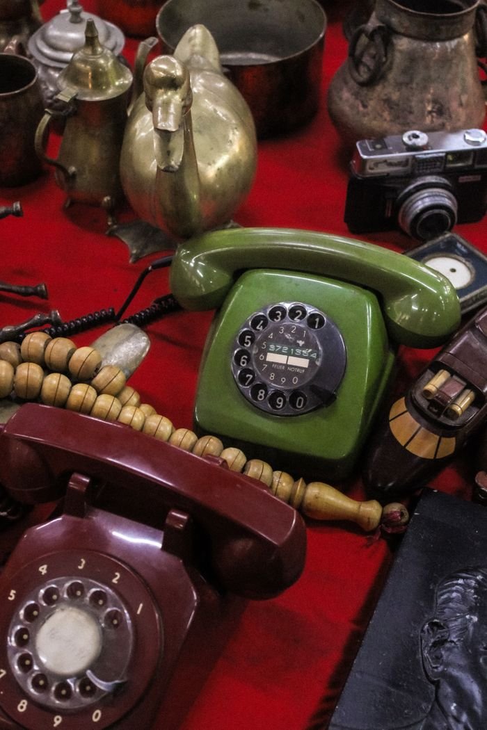 collection-02 A vibrant display of vintage items including rotary phones and brassware on a red cloth at a flea market.
